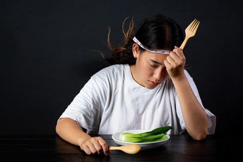 Woman trying to force herself eating salad