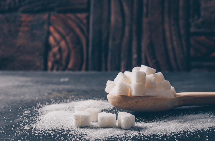 White sugar cubes on wooden spoon with granulated refined sugar sprinkled on table